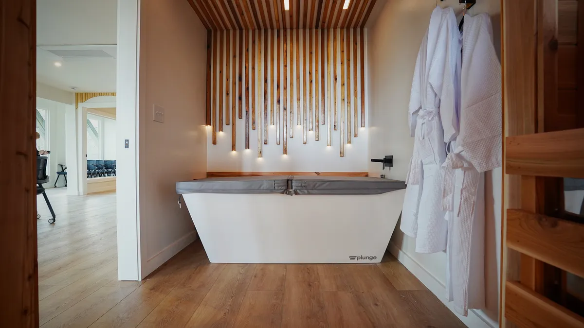 A serene, modern plunge tub set against a wooden slat wall, with plush bathrobes hanging nearby. The space exudes tranquility and feels tailored for immersive self-care and wellness rituals.