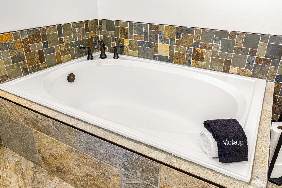 A calming bathroom scene showcasing a bathtub with a tile backsplash, modern faucets, and neatly arranged towels. The space is styled for relaxation and pampering.