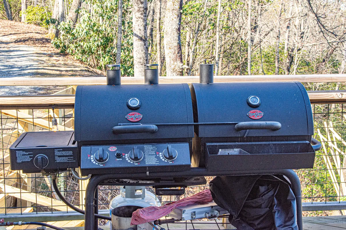 A cheerful exterior scene with a double grill situated on a wooden deck, surrounded by nature. The setup is ideal for group barbecues or cooking competitions, with plenty of space for friends and family to gather and enjoy a meal together outdoors.
