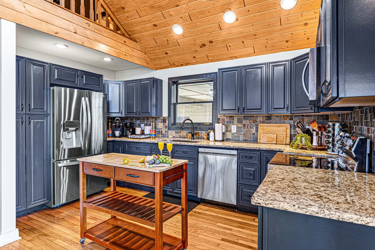 This image features a modern kitchen with granite countertops, stainless steel appliances, and an island cart stocked with fresh fruits. Dark cabinetry provides a rich, inviting atmosphere, while the open layout suggests the kitchen is designed for group interaction and culinary creativity.